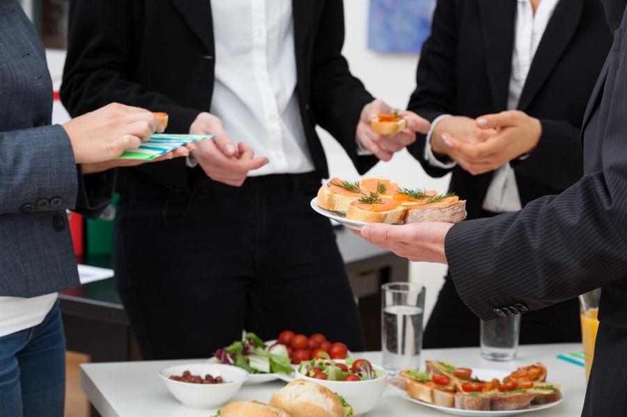 Persone in abiti formali che si scambiano cibo durante un incontro informale.