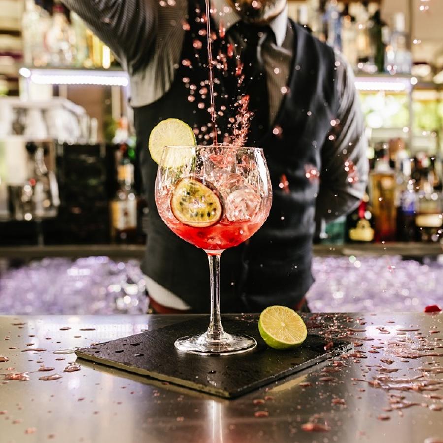 Bartender prepara un cocktail rosso con frutta fresca e ghiaccio in un bicchiere elegante.