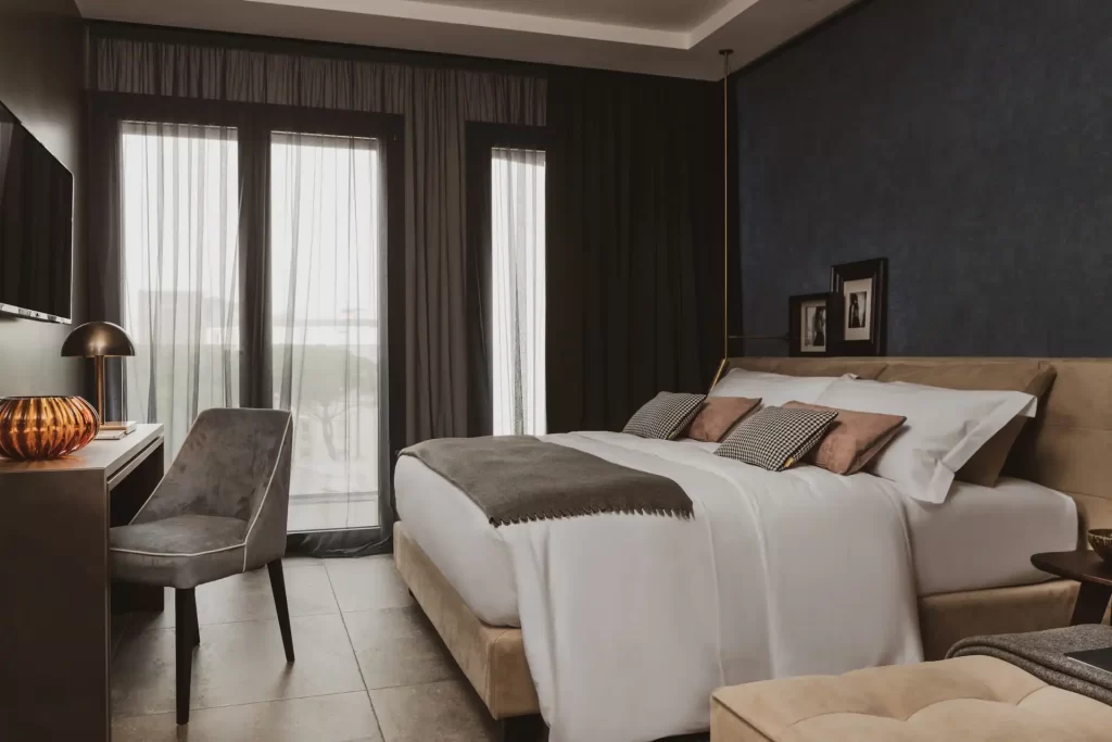 Camera da letto moderna con letto matrimoniale e scrivania accanto a grandi finestre con tende.