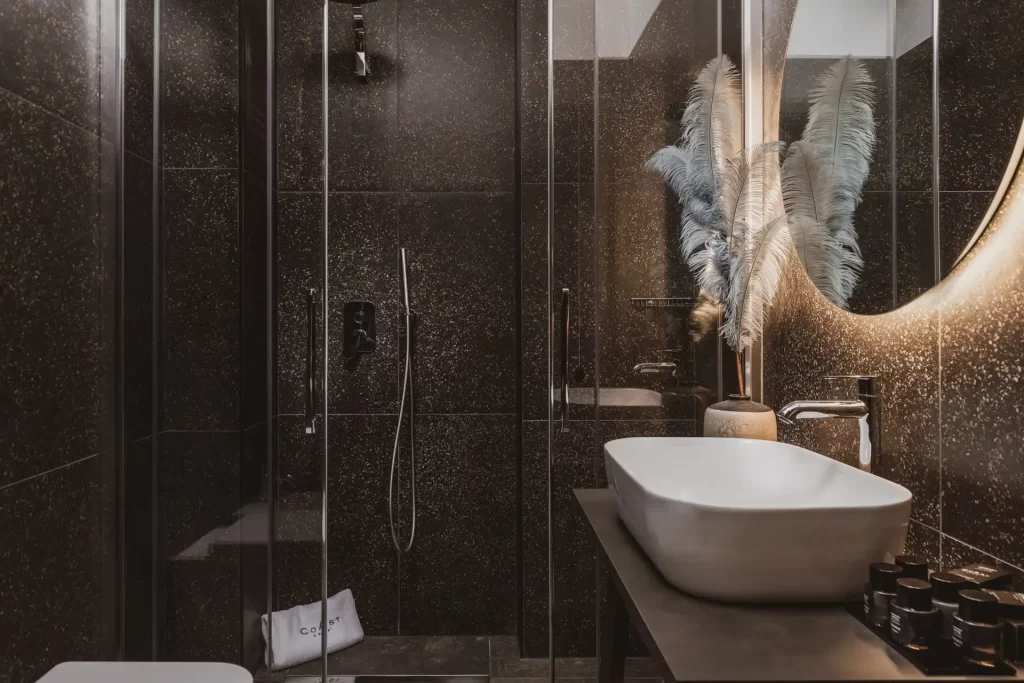 Bagno moderno con pareti scure, lavandino bianco e decorazioni di piume al centro.