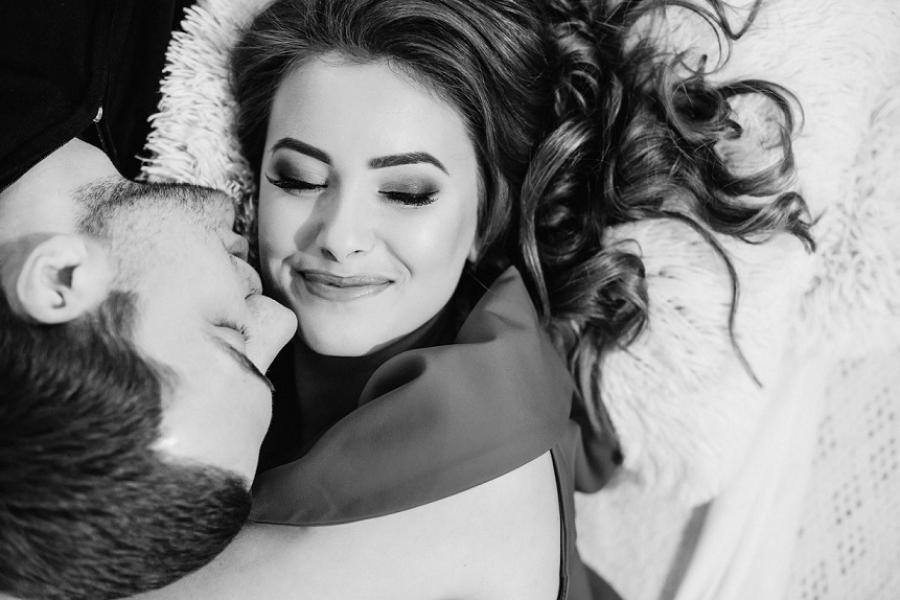 Una coppia sorridente abbracciata su un letto, in un'immagine in bianco e nero.