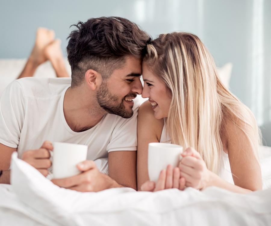 Una coppia sorridente beve caffè a letto.