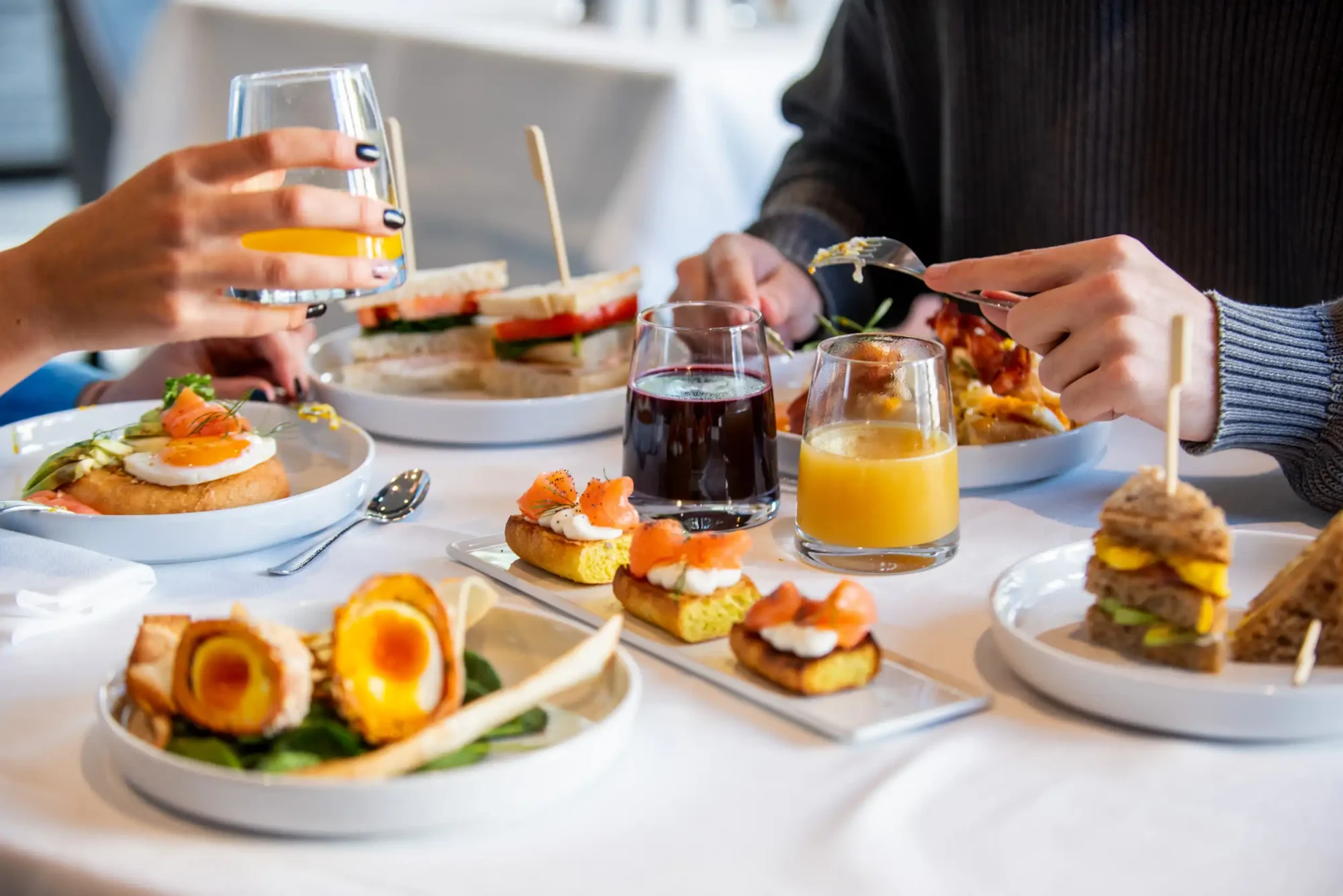 Due persone che condividono un brunch elegante con sandwich, piatti gourmet e bevande.
