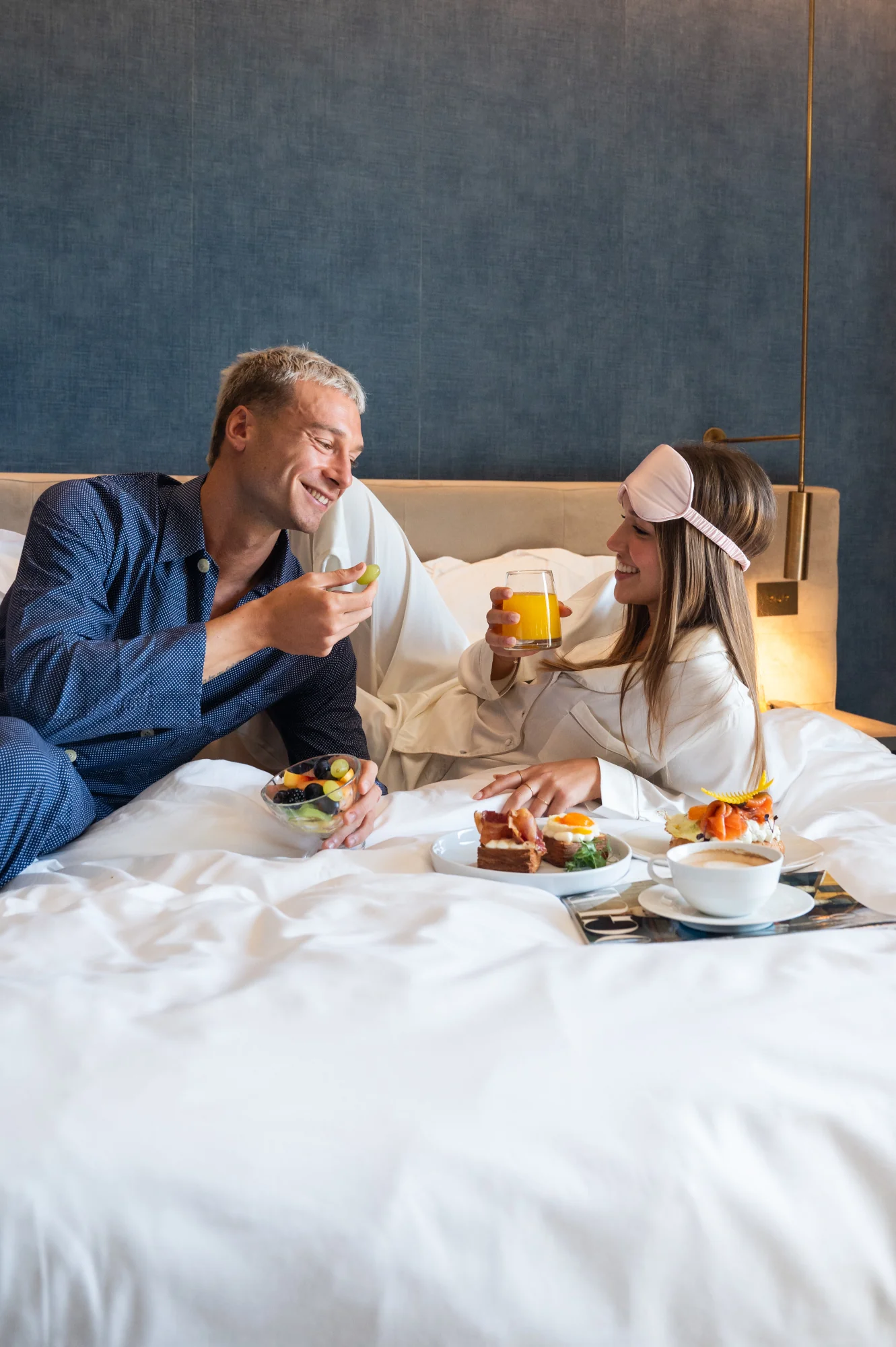 Coppia sorridente fa colazione a letto con frutta e succo d'arancia.