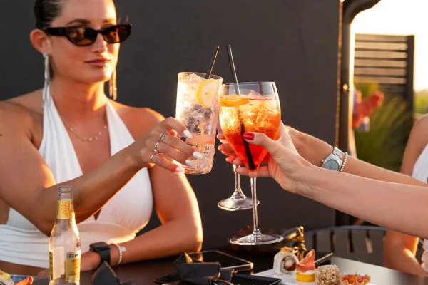Persone che brindano con cocktail durante un aperitivo al tramonto.
