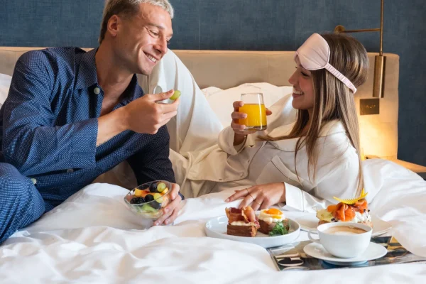 Coppia sorridente fa colazione a letto con frutta e succo d'arancia.