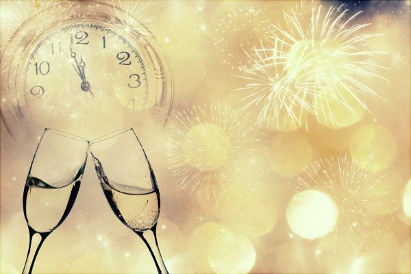 Due calici di champagne brindano con fuochi d'artificio e un orologio che segna la mezzanotte sullo sfondo.
