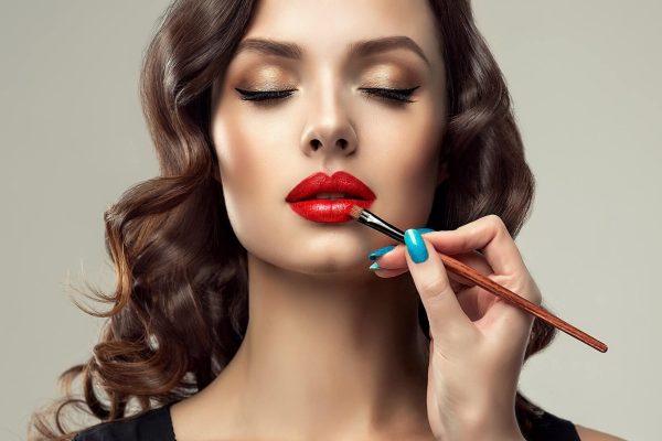 Donna con rossetto rosso applicato da un pennello per trucco.
