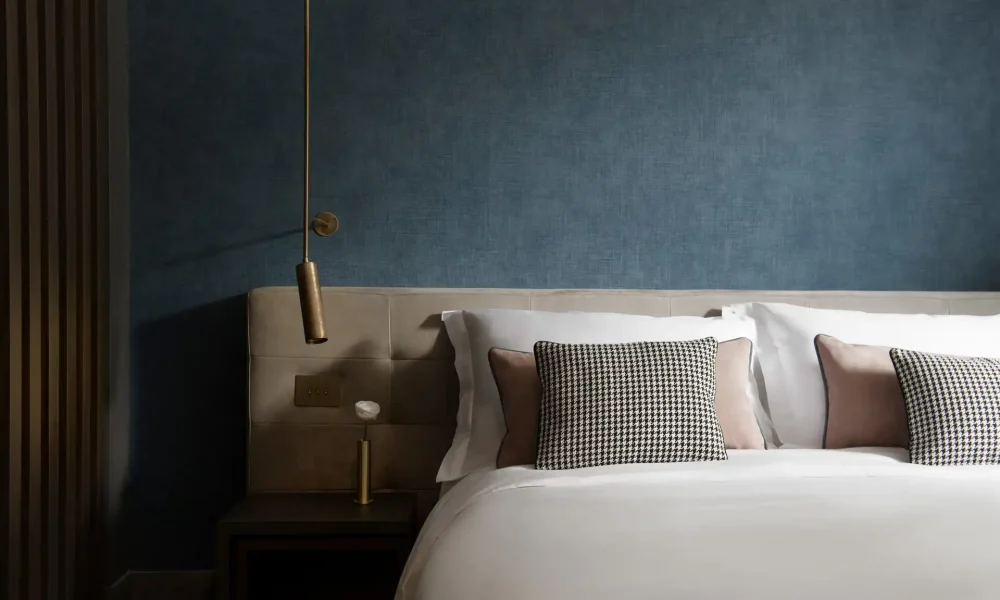 Lit moderne avec des oreillers à motifs et une lampe suspendue dans une chambre au mur bleu.