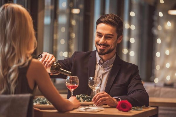Coppia elegante a cena romantica con uomo che versa vino.