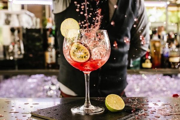 Bartender prepara un cocktail rosso con frutta fresca e ghiaccio in un bicchiere elegante.