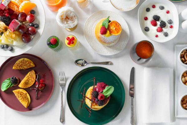 Variegata colazione con frutta, dolci, yogurt e bevande su un tavolo apparecchiato.