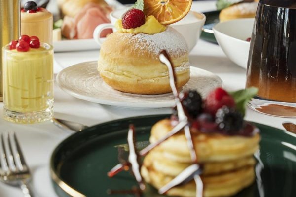 Colazione elegante con pancake ai frutti di bosco, brioche e dolci vari.