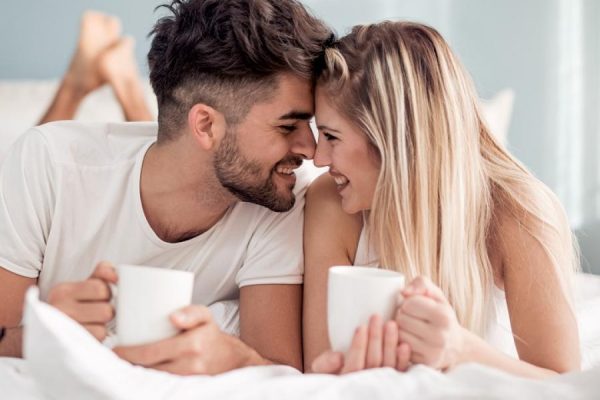 Una coppia sorridente beve caffè a letto.